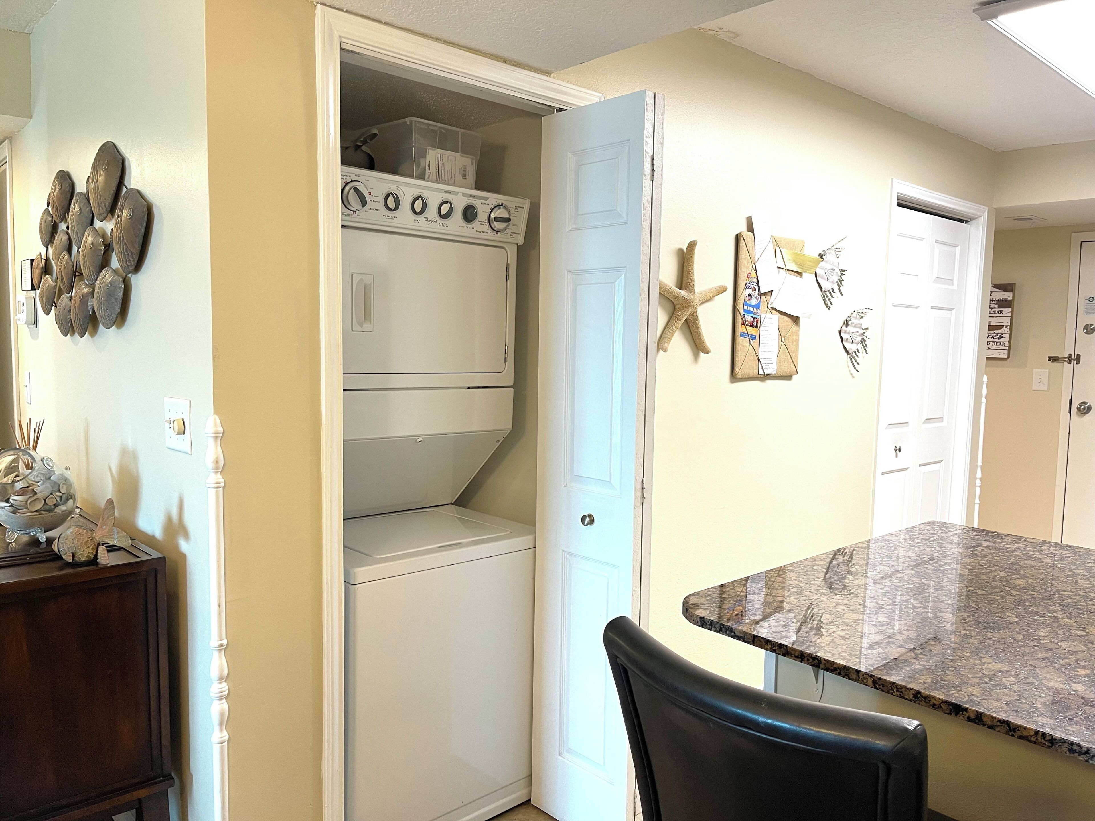 A kitchen with a built-in washer and dryer, a dining area with a granite countertop, and decorative wall art.