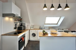 A compact kitchen with a built-in washing machine, a wooden countertop, and pendant lighting.