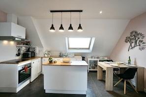 A modern kitchen with a central island, pendant lights, a skylight, and a dining area with a table and chairs.