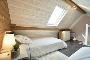 A bedroom with a sloped ceiling, a skylight, a bed, bedside table, lamp, and a small potted plant.