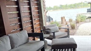Een terras met een bank en twee ronde tafels, houten lamellenwanden en uitzicht op een meer.