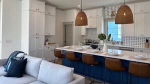 Een moderne keuken met witte kasten, een centraal eiland met barkrukken en hanglampen.