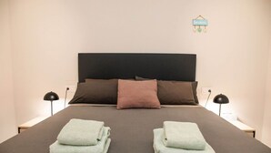 Un lit bien fait, avec une tête de lit sombre, deux lampes de chevet et un panneau accroché au mur.