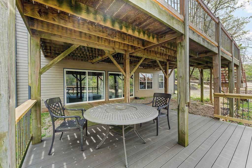 Une terrasse extérieure couverte, dotée d’une table ronde et de chaises, de poutres en bois et offrant une vue sur la maison.