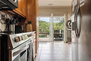 A kitchen with a stove, oven, and refrigerator, leading to a balcony with a view of trees. - Lake Front, Lake Access, Fire Pit, Pet Friendly (Eureka Springs)