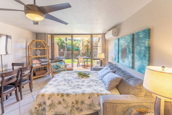 A bedroom with a bed, a sofa, a desk, and a chair. There is a ceiling fan, a lamp, and a window with a view of the outdoors.