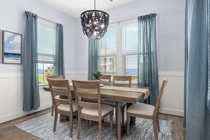 A dining area with a wooden table and chairs, a chandelier, and blue curtains. - Peach, Please-Book 5+ nights get 15% OFF-Bay Side @ Pointe West. 4BD/3.5 BA. (Galveston)