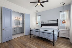 A bedroom with a bed, nightstands, a ceiling fan, and a bathroom with a mirror and vanity. - Peach, Please-Book 5+ nights get 15% OFF-Bay Side @ Pointe West. 4BD/3.5 BA. (Galveston)