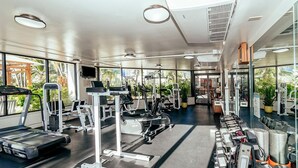 Une salle de sport moderne dotée de divers appareils d’exercice, de grandes fenêtres et d’un intérieur propre et bien éclairé.