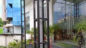 A modern building with a glass facade, outdoor seating area, and potted plants. - Hotel Autumn Crocus (Guwahati)