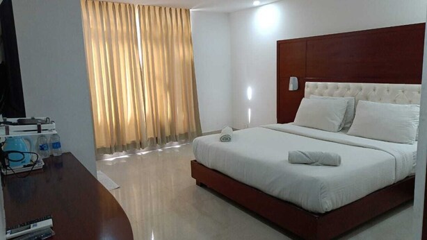 A hotel room with a large bed, a wooden desk with a flat-screen TV, and a window with curtains. - Hotel Autumn Crocus (Guwahati)