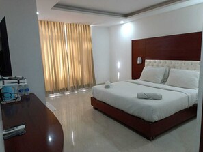 A hotel room with a large bed, a wooden desk with a flat-screen TV, and a window with curtains. - Hotel Autumn Crocus (Guwahati)