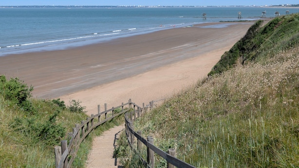 Une plage côtière avec une promenade en bois qui mène au bord de l’eau.