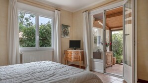 Une chambre à coucher avec un lit, un téléviseur posé sur une table de chevet en bois et une porte-fenêtre coulissante donnant sur un balcon.