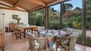 Un coin repas aménagé avec des meubles en osier, une table dressée pour quatre personnes et de grandes fenêtres donnant sur le jardin.