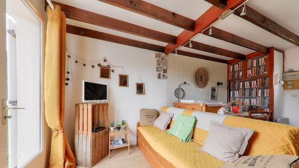 Um quarto aconchegante com uma cama, uma estante de livros, uma televisão e uma janela com cortinas.