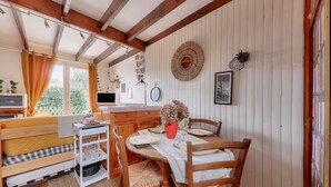 Uma sala de jantar acolhedora com uma mesa de madeira posta para dois, um banco com almofadas e um objeto decorativo fixado na parede.