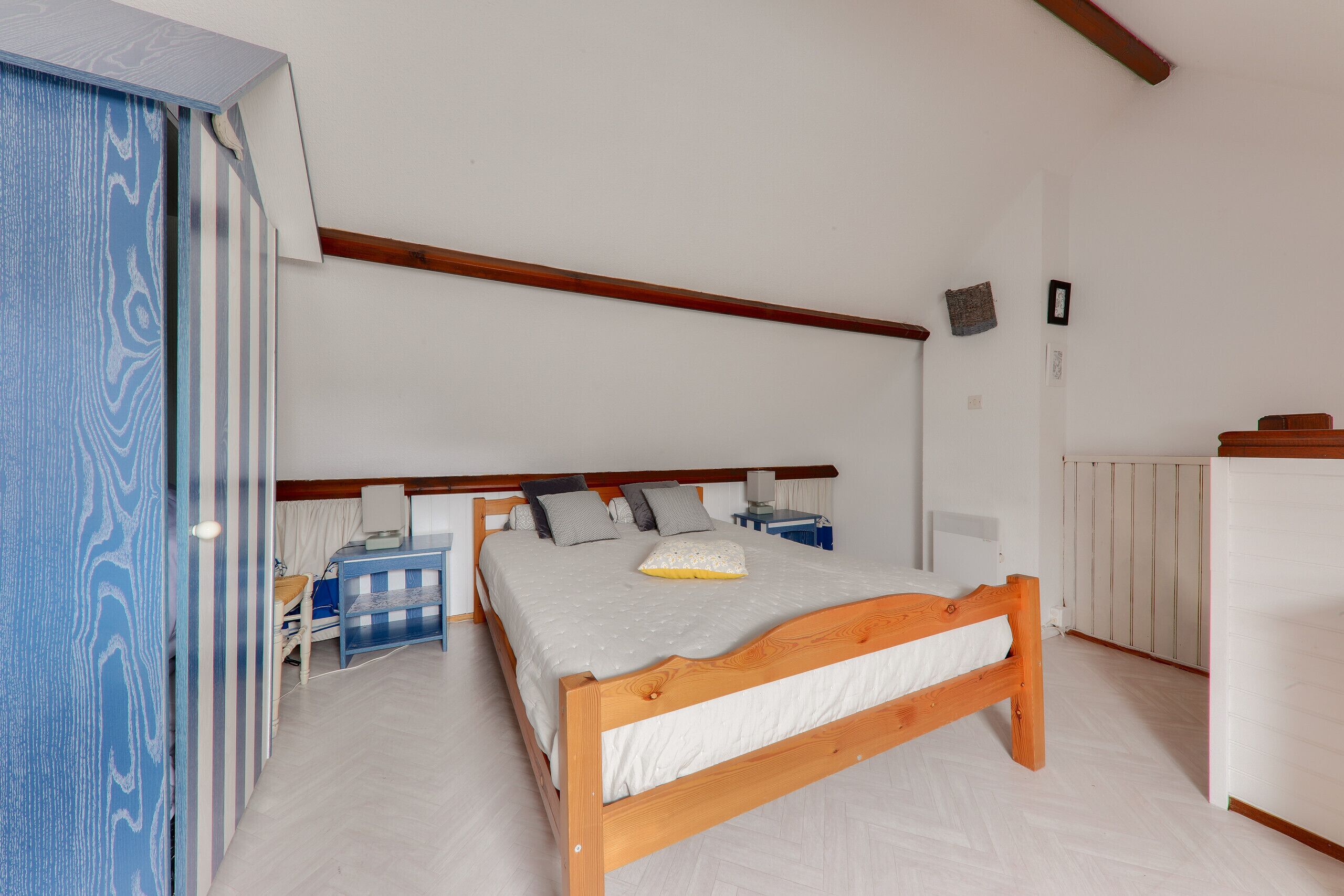Een slaapkamer met een houten bed, nachtkastje, bureau en garderobe.