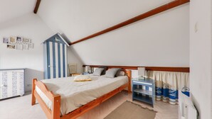 Quarto com cama de madeira, um pequeno armário azul e branco listrado, uma escrivaninha e um radiador.