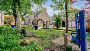 Een tuin met een gebouw van baksteen, een blauwe waterpomp en een stenen boog.
