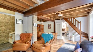 Een ruime woonkamer met een stenen muur, houten balkenplafond, een leren fauteuil, een bank en een trap naar een hoger niveau.