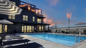 A rooftop pool area with lounge chairs and umbrellas, a pool, and a building with string lights. - Spacious Oasis w/ Pool, Gym, & Stunning City Views (Birmingham)