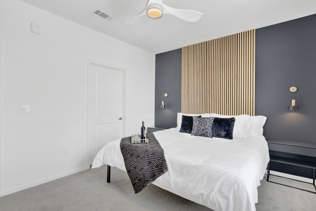 A modern bedroom with a bed, bedside tables, a ceiling fan, and a wall-mounted light fixture.