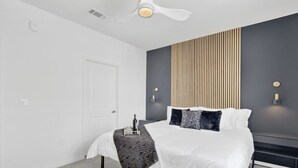 A modern bedroom with a bed, bedside tables, a ceiling fan, and a wall-mounted light fixture. - Spacious Oasis w/ Pool, Gym, & Stunning City Views (Birmingham)