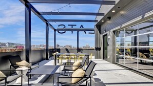 A rooftop terrace with outdoor seating, a view of the city, and a building entrance. - Spacious Oasis w/ Pool, Gym, & Stunning City Views (Birmingham)