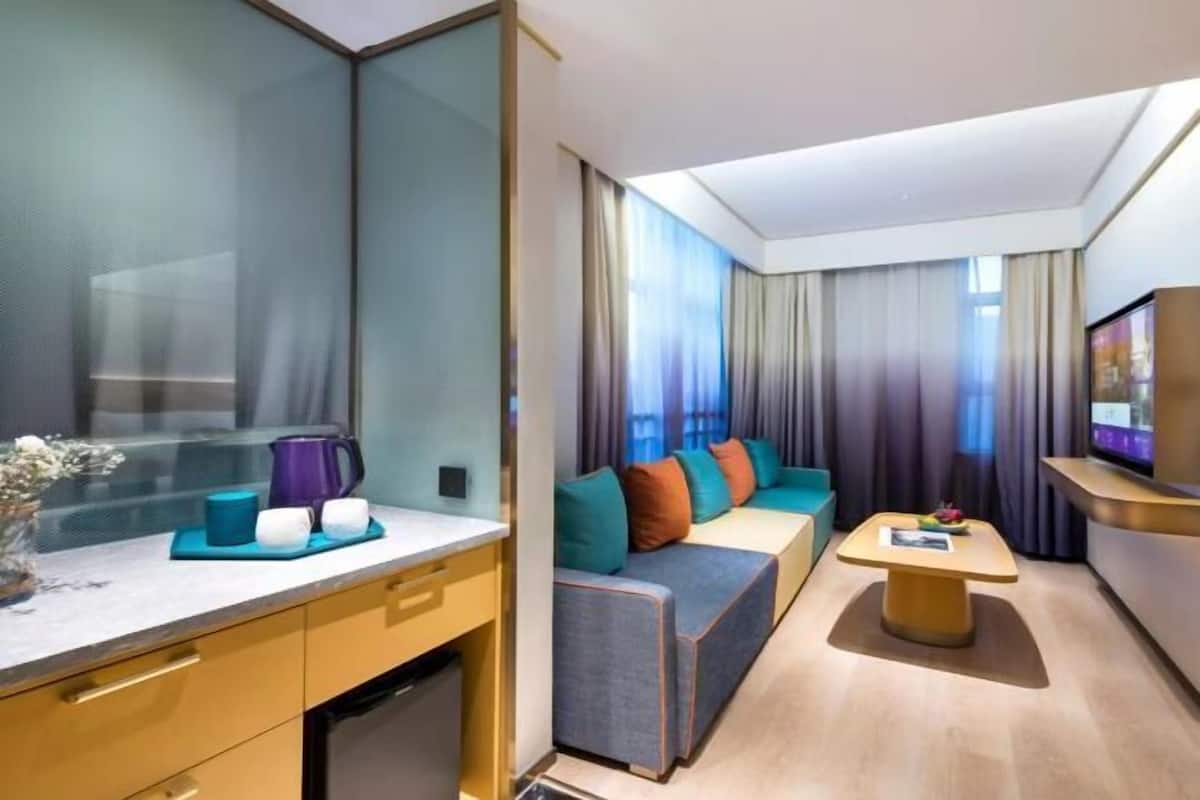 Una habitación de hotel moderna con sofá, una mesita, televisión y minibar.