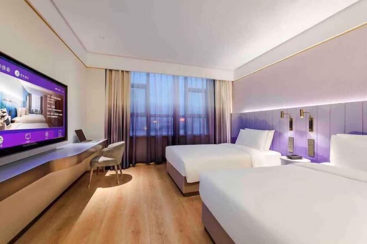 Una habitación de hotel moderna con una televisión de pantalla plana grande, dos camas, un escritorio y una silla.