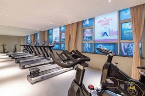 A gym with stationary bikes and treadmills, large windows with digital displays, and a modern interior design.