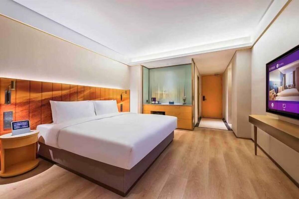 Habitación de hotel moderna con una cama grande, una mesita de noche con una computadora portátil, un televisor en la pared y un cabecero de madera.