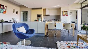 Une cuisine moderne avec un îlot central, un coin repas avec une chaise bleue et un espace de vie avec un fauteuil bleu.