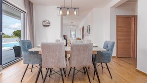 Un coin repas comprenant une table en bois, quatre chaises rembourrées et un luminaire suspendu.
