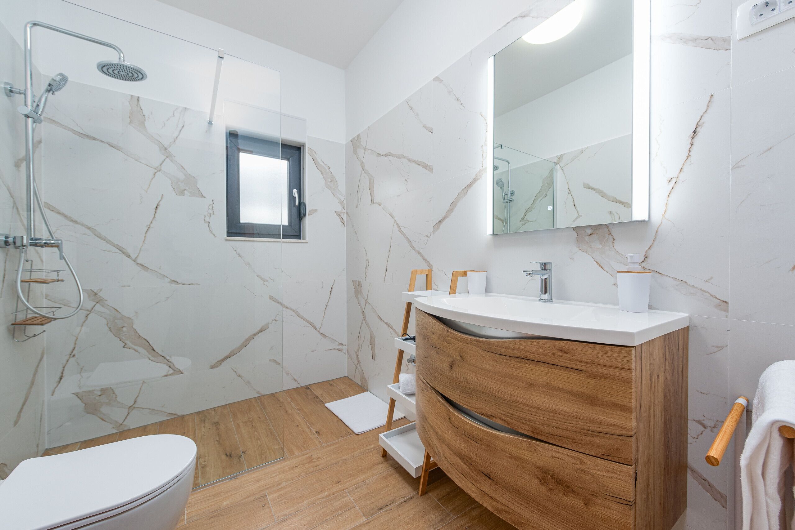 Ein modernes Badezimmer mit Marmorwand, Holzwaschtisch und einer Duschkabine aus Glas.