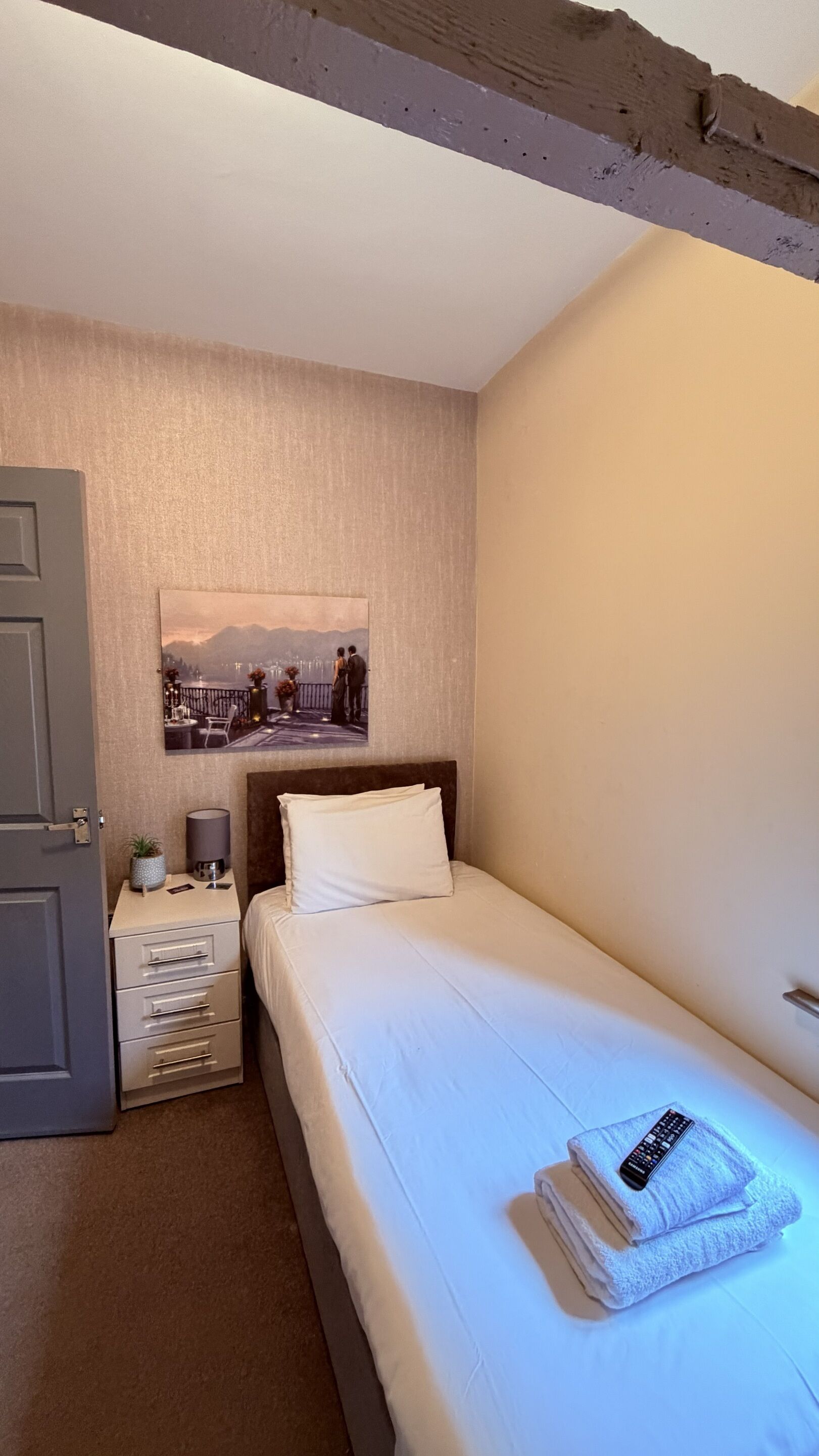 A neatly made bed with a pillow, a bedside table with a lamp, and a framed picture on the wall.