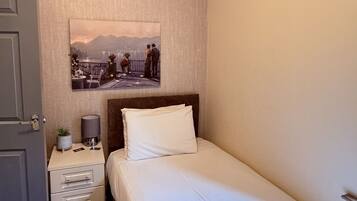 A neatly made bed with a pillow, a bedside table with a lamp, and a framed picture on the wall.