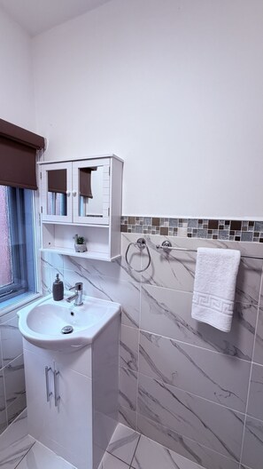 Un baño moderno con un lavabo blanco, tocador y paredes cubiertas de mármol.