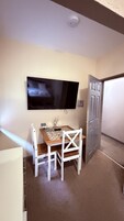 Una habitación pequeña con un televisor en la pared, una mesa con sillas y una puerta.