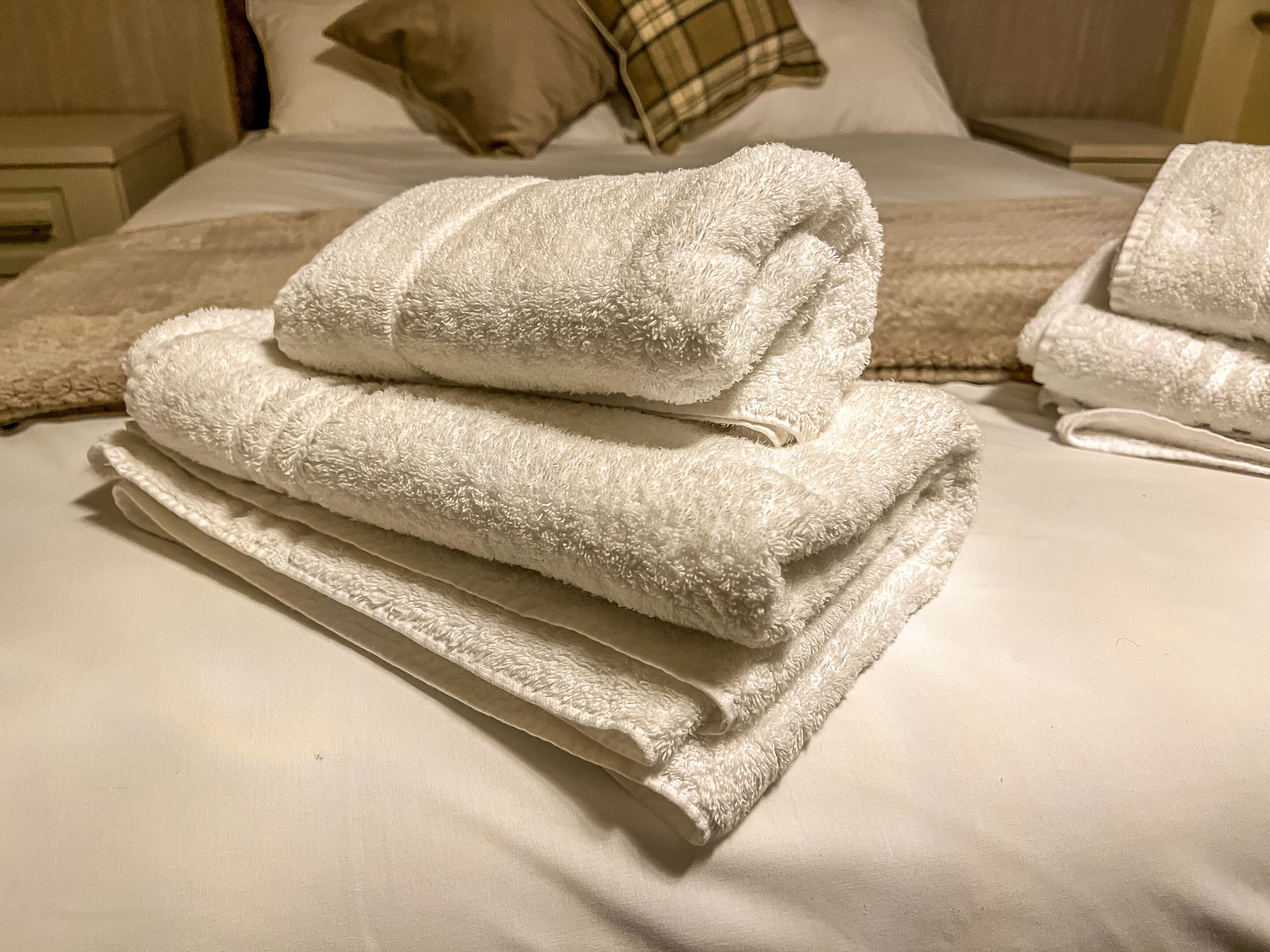 Un lit bien fait, avec une couette blanche et plusieurs serviettes pliées.