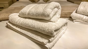 Un lit bien fait, avec une couette blanche et plusieurs serviettes pliées.