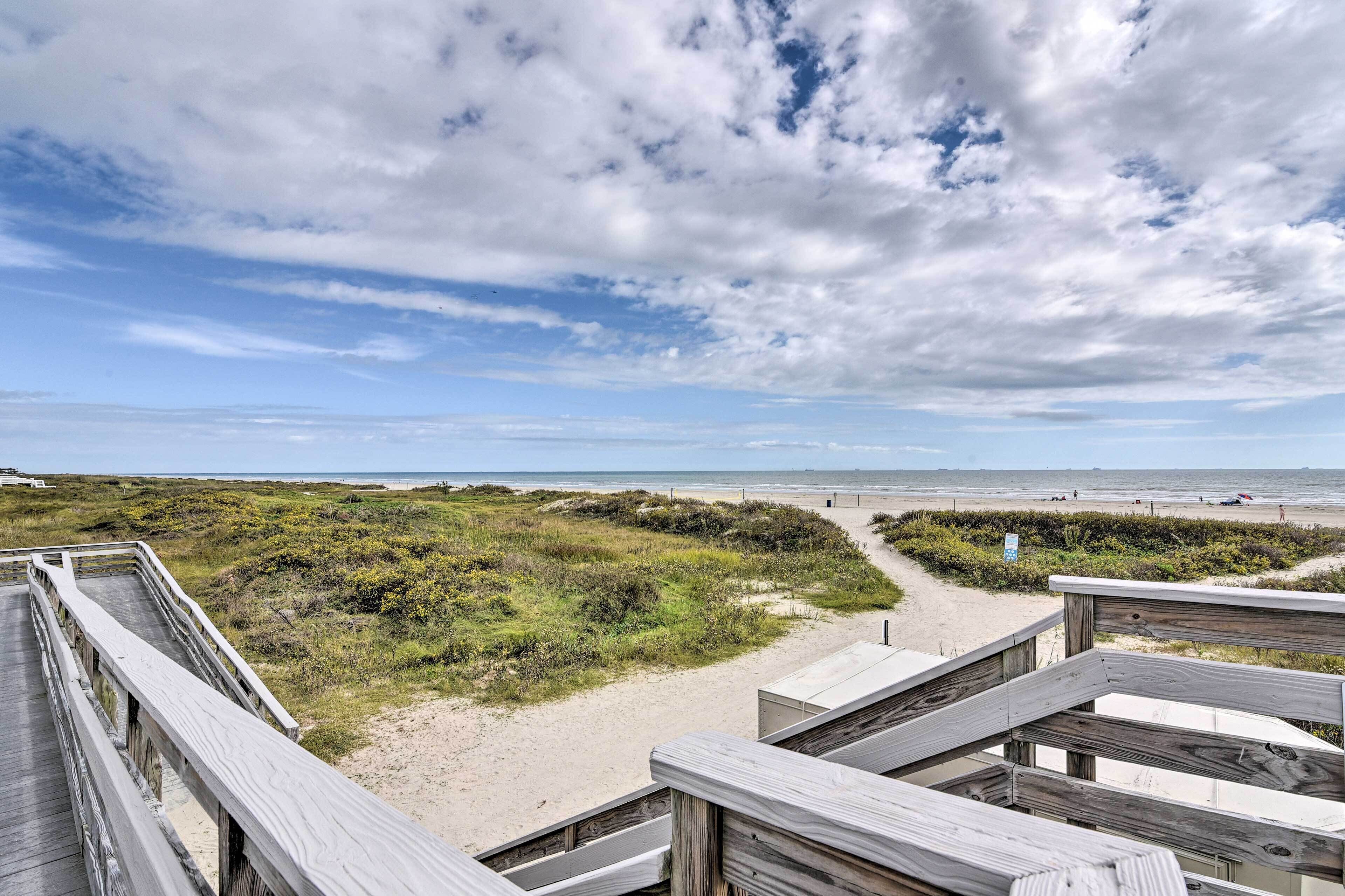 A wooden boardwalk leading to a beach with sandy dunes and a clear sky.