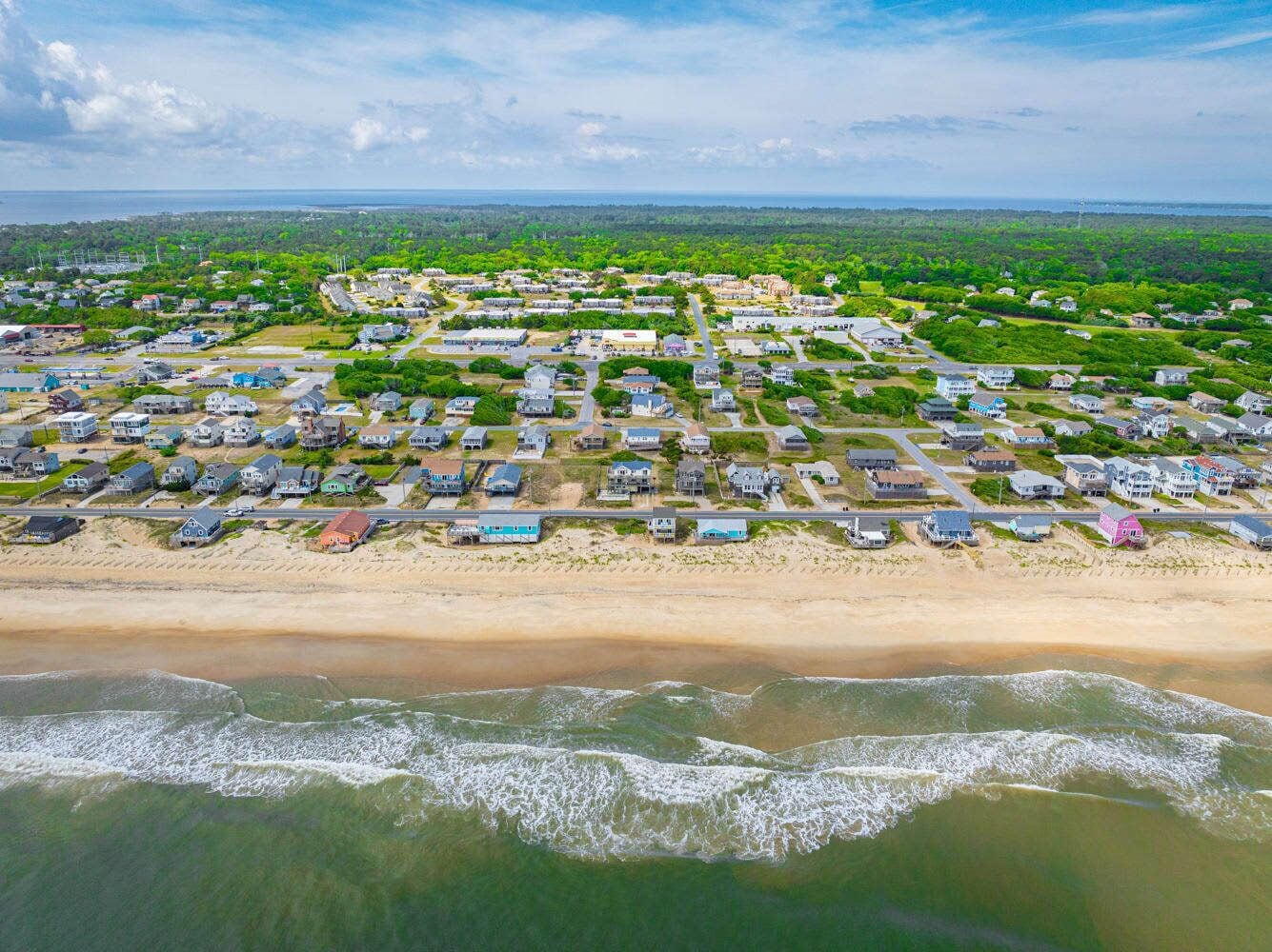 An aerial view of a coastal residential area with houses, a beach, and a view of the ocean.