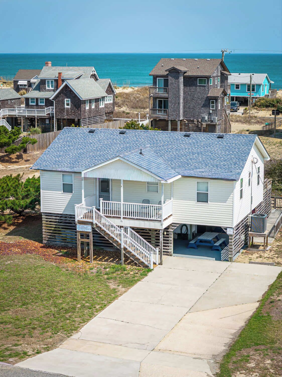 Una casa frente a la playa con un porche cubierto, una pequeña terraza y vista al océano.