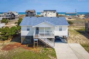 Een huis aan het strand met een overdekte veranda, een trap en uitzicht op de oceaan.