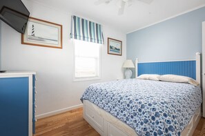 Een slaapkamer met een bed, een dressoir, een raam en twee ingelijste foto’s aan de muur.
