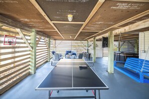 Een tafeltennistafel in een ruimte met een basketbalring, houten balken en een blauwe bank.