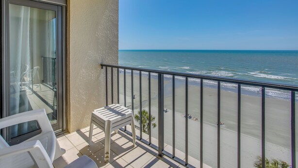 Un balcon avec vue sur la plage, une porte vitrée et une petite table.