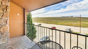 Un balcon avec un mur en pierre, une rambarde en métal et une vue sur un parking rempli de voitures.